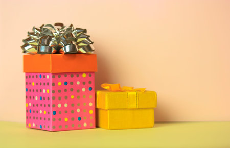 Pink gift box with a silver bow and a small yellow gift box on a soft pink pastel nude background....