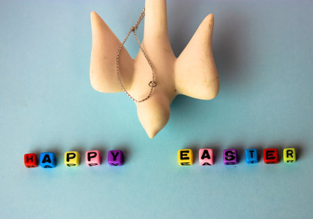 A Happy Easter inscription of multicolored beads and a white ceramic bird on a delicate blue...
