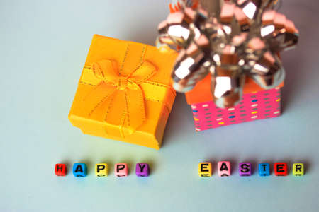 A Happy Easter inscription of multicolored beads, a yellow and pink gift boxes on a delicate blue or white background. Easter background flatly.の写真素材