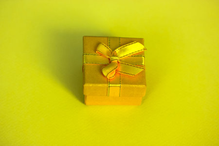 Bright yellow gift box with a bow isolated on a yellow background. Top view, flatly. Holiday...