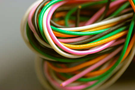 A bundle of multicolored electrical, car, computer, telephone wires twisted together background. Orange, green, pink, white cables on gray background. Computer networks, electrician services concept.の写真素材