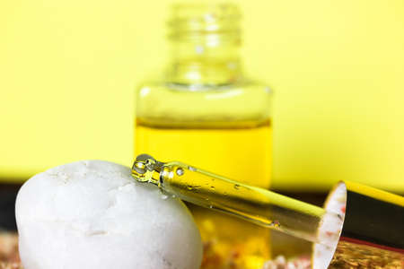 Golden yellow oil serum in pipette. Natural organic cosmetic product for facial skincare and skin regeneration. Transparent glass bottle with liquid skin care sunscreen oil. Sea theme, pebbles, sand.の写真素材