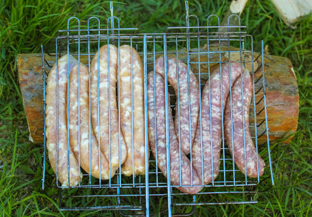 Raw sausage on a BBQ grill toppers top view, flatly, Preparing fresh meat outdoors. Picnic in the...