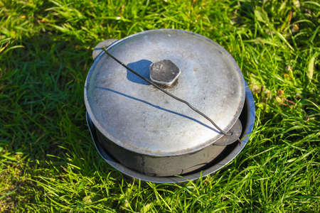 Camping gray aluminum cauldron on a green grass on a sunny summer day flatly. Cooking in nature during a camping trip. Traveling, tourism, picnic cooking, cooking at the stake in a cast iron cauldron.の写真素材