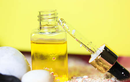 Pipette with liquid oil in a glass transparent bottle to moisturize a cuticle. Essence for skin care on yellow background. Hyaluronic serum. Suntan oil. Cosmetic serum. Cosmetology, treatment concept.の写真素材