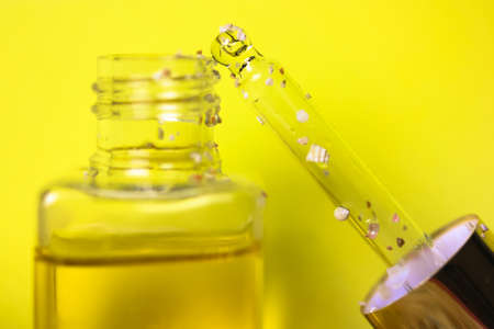 Pipette with liquid oil in a glass transparent bottle to moisturize a cuticle. Essence for skin care on yellow background. Hyaluronic serum. Suntan oil. Cosmetic serum. Cosmetology, treatment concept.の写真素材