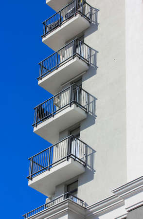 The exterior of a modern luxury apartment building in the city. Balconies of a newly built house with black metal grilles and contrast shadows on a sunny day. Multistory building against a blue sky.の写真素材