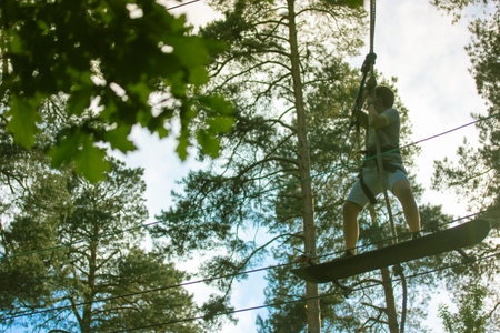 A teenager flies a skateboard in a rope park using extreme sports equipment. A ropes course high up...