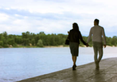A couple in love walking along the waterfront, holding hands. Beautiful young man and girl from the back in defocus against light blue sky. A stroll through the city. A first date. Place for text.の写真素材