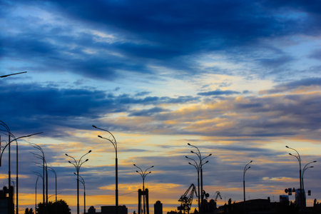 Contrasting silhouettes of street lamps against a bright orange and dark blue cloudy sky at sunset....