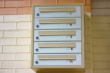 Gray-yellow multi-section metal mailbox against the beige brick wall. Apartment numbers 3, 4, 7, 8,...