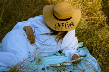 A young lady, woman in a straw hat with a written word Offline lies on a plaid with a book. Reading...