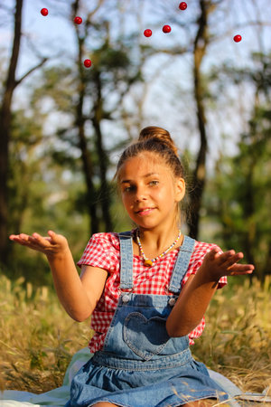 Girl with cherries in the orchard at summer. Pretty teenage mestizo girl 10-13 years old tossing up...
