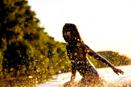 Silhouette of happy little girl playing in a water. Teenage kid frolics, has fun, jumps in the sea,...