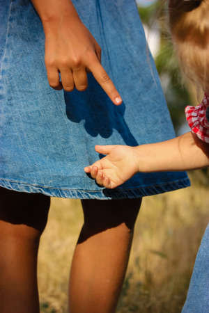 A little light-skinned infant girl of 2-3 years old reaches out her hand to her older sister, a dark-skinned tan girl. Sisters outdoors on a sunny day. Contrast shadows. Two little infant girls cousinの写真素材