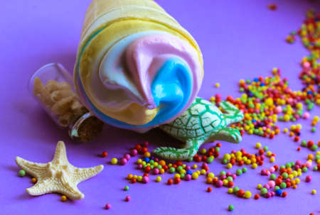 Colorful ice-cream in a waffle cup, a turtle and a starfish on a purple background flatly. Trendy colors of summer 2021 - pastel blue, pink, yellow. High-calorie tasty sweet snack. Summer food conceptの写真素材