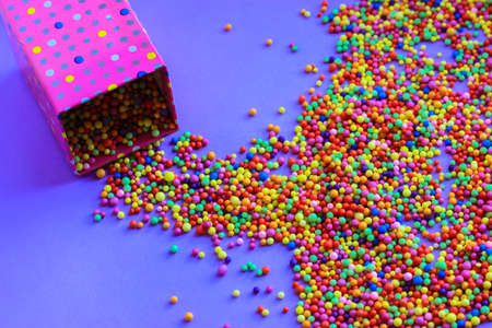 Foam balls of different colors scattered on a table from a pink polka dot gift box. A beautiful festive purple background flatly. Holiday, birthday, anniversary, gift, present, party, fun concept.の写真素材