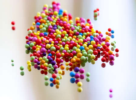 Foam polystyrene round bright colorful beads are reflected on a surface of a glass, mirror. Multicolored pearls floating down, hanging in the air. Foam spherical background. Celebration, fun concept.の写真素材