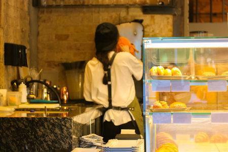 A back view female barista prepares orange fresh juice, serving a customer. An unrecognizable cafe...