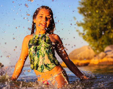Beautiful smiling happy teenage girl frolicking in a sea at summer. Splashing, dripping water. A cute kid at a children's camp on summer holiday have fun outdoors. Childhood concept. Positive emotionsの写真素材