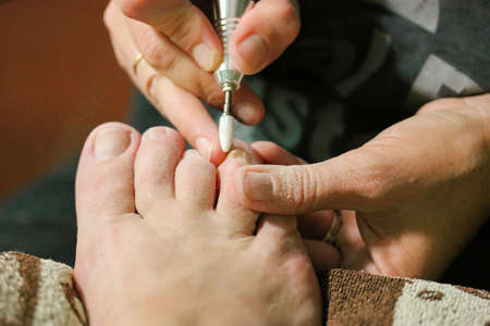 Apparatus pedicure with an electric machine in a beauty salon. Professional manicurist polishing the nail plate, cuticle. Women's feet close up. A pedicure apparatus with a drill. Nail care concept.の写真素材