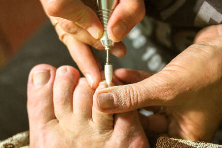 Apparatus pedicure with an electric machine in a beauty salon. Professional manicurist polishing the nail plate, cuticle. Women's feet close up. A pedicure apparatus with a drill. Nail care concept.の写真素材