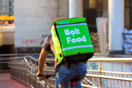 Kyiv, Ukraine. May 1, 2021. A worker of a Bolt Food delivery service, company rides bike on a city street. A cyclist with a green backpack delivering fast foods, meals to a customer. Selective focus.のeditorial素材