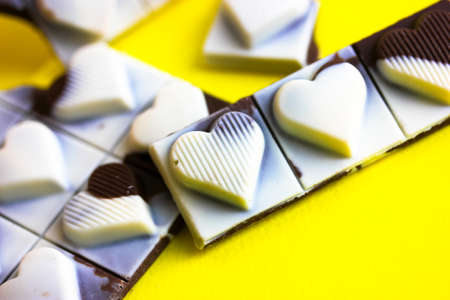 Milky dark chocolate bar with hearts on each slice top view. Broken black white pieces on yellow background flatly. World Chocolate Day. Sweet, calorie unhealthy food. Valentine's day and love conceptの写真素材
