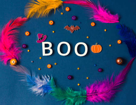 Boo word, colorful feathers on dark gray background. Halloween holiday concept. Bat, orange jack o lantern pumpkin, witch hat symbols. Party greeting card. Copy space, place for text. Flatly top view.の写真素材