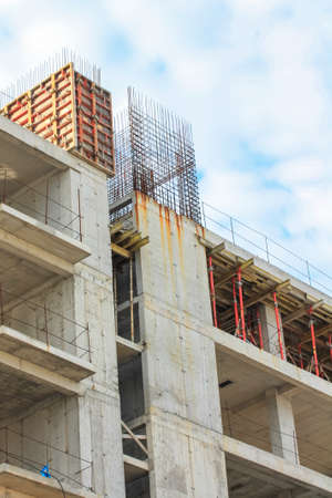 Concrete construction of a new high-rise apartment building. An unfinished buildings facade view from outside. Residential complex exterior. Real estate. Slabs, walls, metal rods. Vertical photographyの写真素材