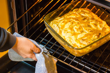 A woman's hand pulls a glass container with a traditional American apple pie from the oven. Baking at home. A cooking process hot food dessert for Thanksgiving Day. Baking pies at fall season.の写真素材