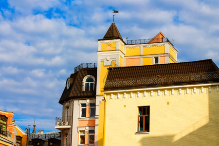 Kyiv, Ukraine. July 9, 2021. Beautiful bright yellow buildings, castle spires against blue cloudy sky at sunny day. Fabulous little town in a historic center. Residential and commercial real estate.のeditorial素材