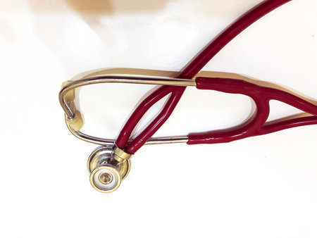 Red stethoscope is lying on white table view from above. Medical diagnostic device for listening to...