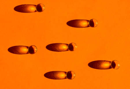 Gold colored fish oil pills, tablets, omega 3 gelatin capsules lie on orange table leaving contrasting long shadows flatly. Medical, health care, medicine treatment minimalistic monochrome background.の写真素材