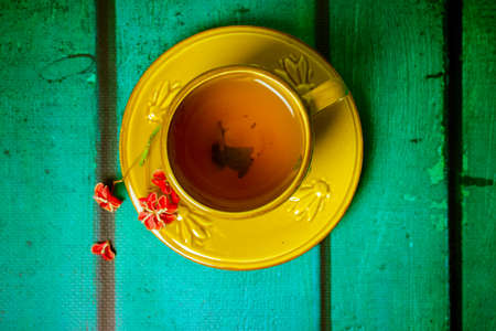 Yellow cup with black aromatic tea inside, red spindle shrub flower on saucer view from above. Mug stands on wooden green table top view. Beautiful composition flatly with place for text. Hot beverageの写真素材