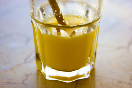 A faceted glass with orange juice inside stands on a marble table in a cafe or restaurant. A morning...