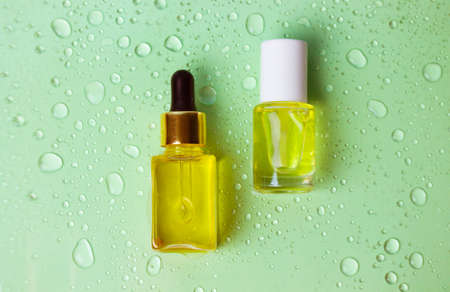 Containers, packaging for cosmetics. Glass bottle pipette dropper of essential oil for face, body on green water drops background. Care cosmetics. Natural eco massage oil. Oil for cuticle moisturizingの写真素材