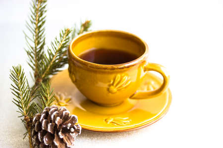 Yellow ceramic coffee cup on a saucer on white table. Christmas tree branch coneの写真素材