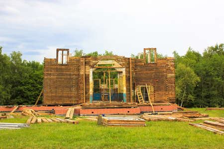 Building a residential wooden house. Facade of unfinished building without roof. A process of disassembling or assembling a hut in nature against green grass, forest. Construction or renovation.の写真素材