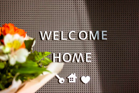 Flowers bouquet in bloom petals in defocus and the inscription text WELCOME HOME on a gray background. Sweet home, housewarming. Key, house, heart symbols.の写真素材