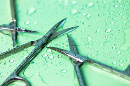 Sharp titanium manicure scissors for trimming cuticles on green turquoise background with water...