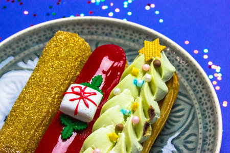 Festively decorated gold, green, red eclairs in New Year's style 2022 lying on round gray plate top...