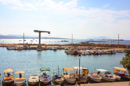 Crete, Greece, June 7, 2019. Waterfront with boats parked in a harbor in a bay. Parking lot for maritime vehicles. Mediterranean Sea at summer day. Empty coastline. Hills, low mountains on the horizonのeditorial素材