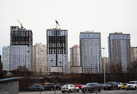 Kyiv, Ukraine. January 8, 2022. Unfinished multi-story apartment buildings, construction cranes against gray sky. A process of construction of tall buildings. Urban cityscape. Cars parked in a parkingのeditorial素材