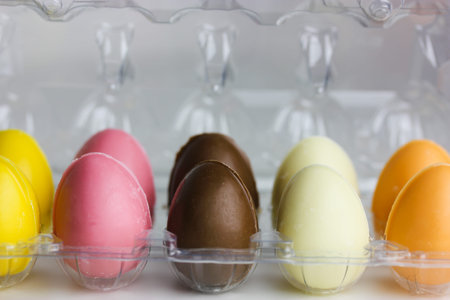 Multicolored Easter chocolate eggs in thermoplastic egg packaging on a white background. Treats for children, kids in spring holiday. Colored sweets on the table. Easter concept. Festive composition.の写真素材