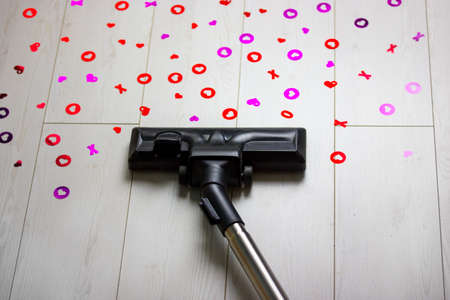 Vacuum cleaner cleans white floor from scattered heart-shaped confetti from poppers cannons. Cleaning house after Valentine's Day party on February 14 is over. I don't love you anymore concept.の写真素材