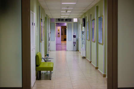 Kyiv, Ukraine. June 1, 2020. A green sofa for waiting patients in a long, empty hospital corridor. A hallway in a modern medical facility with white closed doors. Artificial lighting indoors. Interiorのeditorial素材