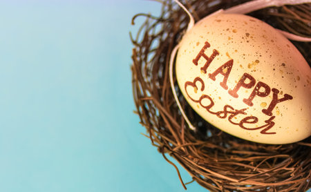 Egg in bird's nest with text Happy Easter on light blue background with space for text on the left....