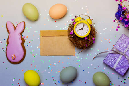 Easter decorations composition top view. Easter symbols - pink bunny, colorful chicken eggs, bird's nest, yellow alarm clock, brown envelope letter. spring holidays. Happy Easter background flat.の写真素材