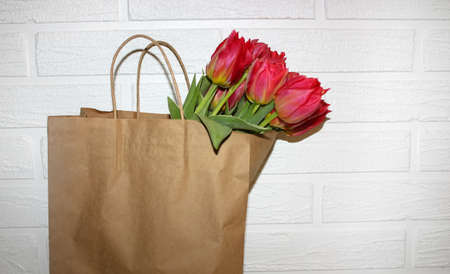Bouquet of fresh pink yellow tulips in eco paper bag on white brick wall background. Congratulations on Mother's Day Grandmother's Day. spring bulb flowers bloom. Seasonal blossoming. floral wallpaperの写真素材